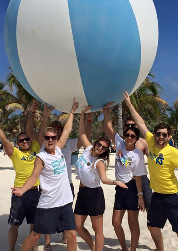 a group of staff on the beach holding a giant beach ball above their head