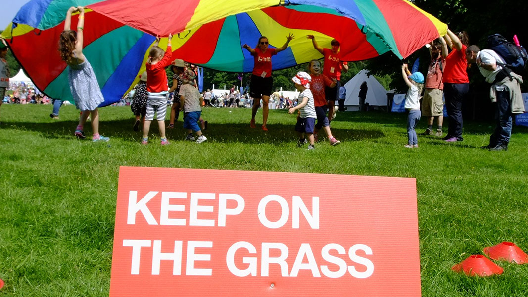 active_002 children taking part in parachute games with a sign saying 'keep on the grass' in the forefront