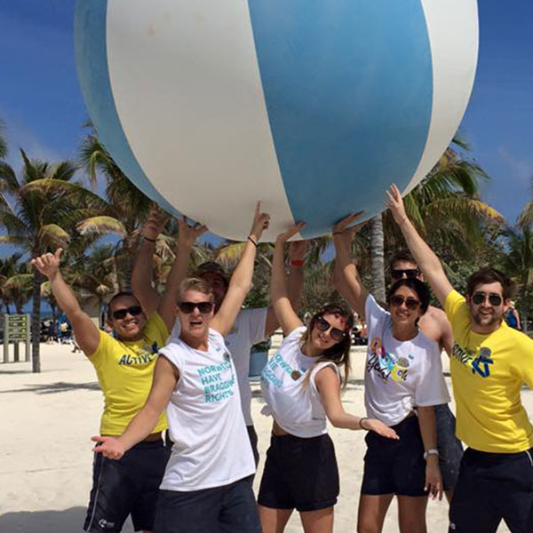 a group of staff members on the beach holding a giant beach ball in the air